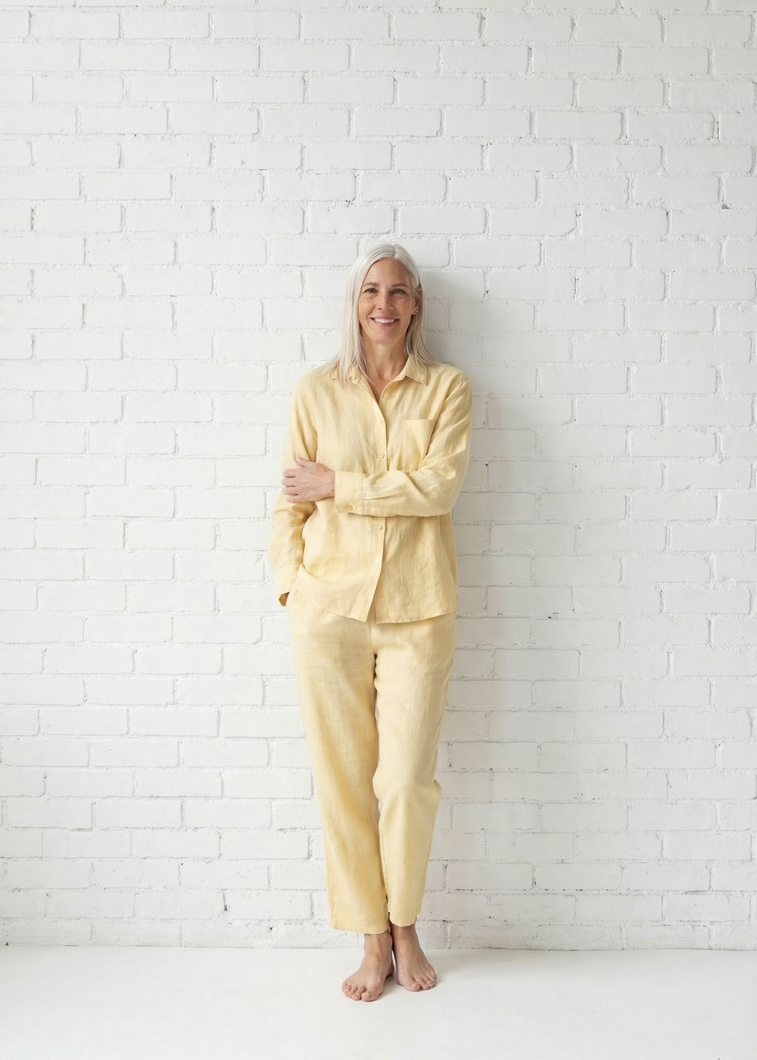 Person wearing a light yellow outfit standing against a white brick wall.