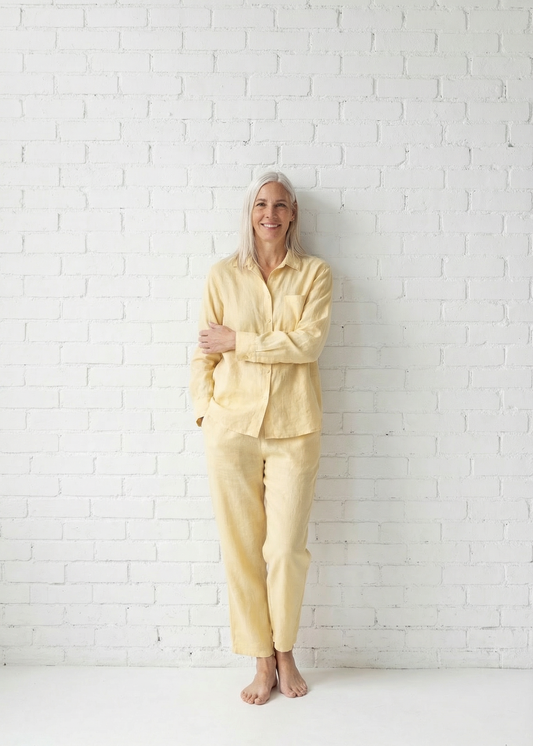 Person wearing a light yellow outfit standing against a white brick wall.