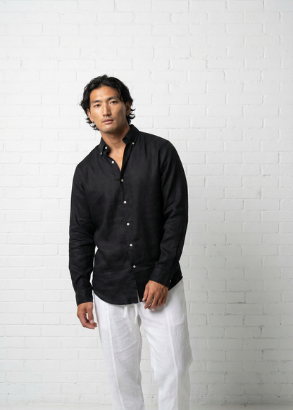 Man wearing a black shirt and white pants against a white brick wall