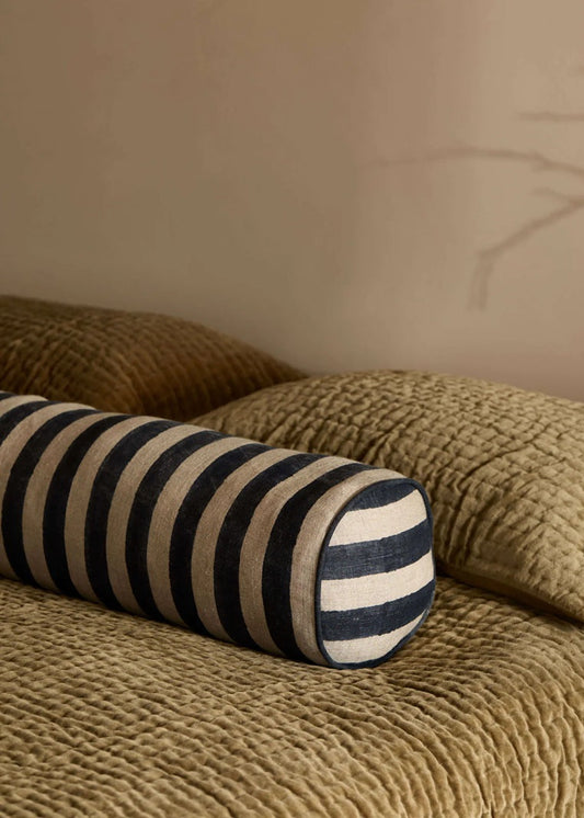 Striped cylindrical pillow on a textured beige sofa against a neutral wall.
