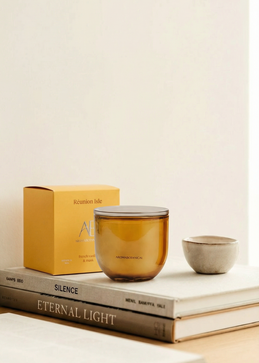 Brown glass candle on a stack of books with a yellow box labeled 'Eternal Light' on a light beige background.