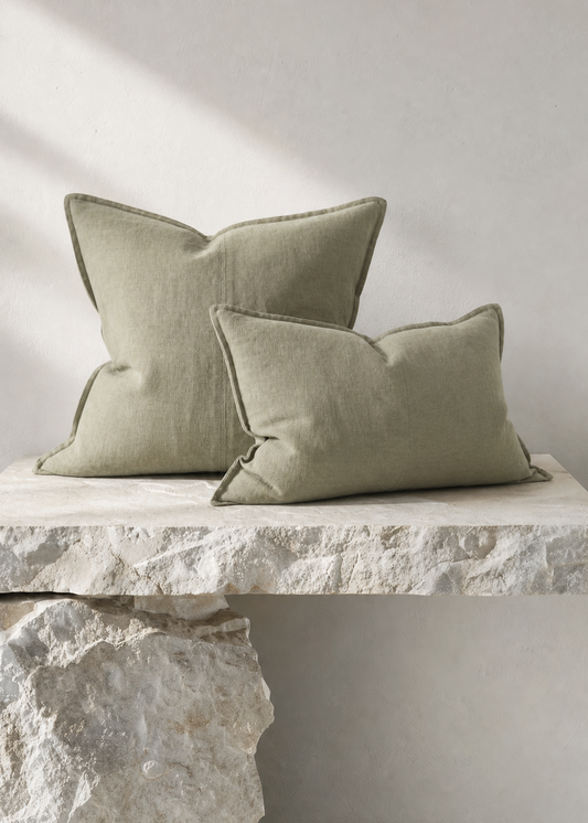 Two textured linen throw pillows in a muted sage green color, styled on a rustic stone bench against a neutral light gray wall.