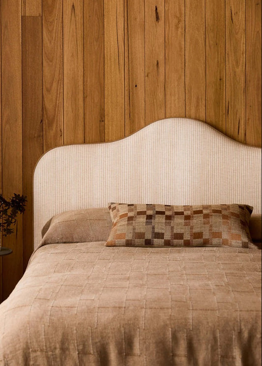 Bed with beige bedding and a patterned pillow against a wooden wall.