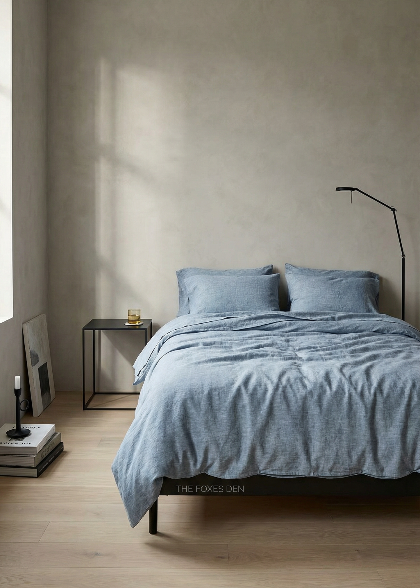 Minimalist bedroom with a bed covered in blue bedding, a side table, and a lamp.