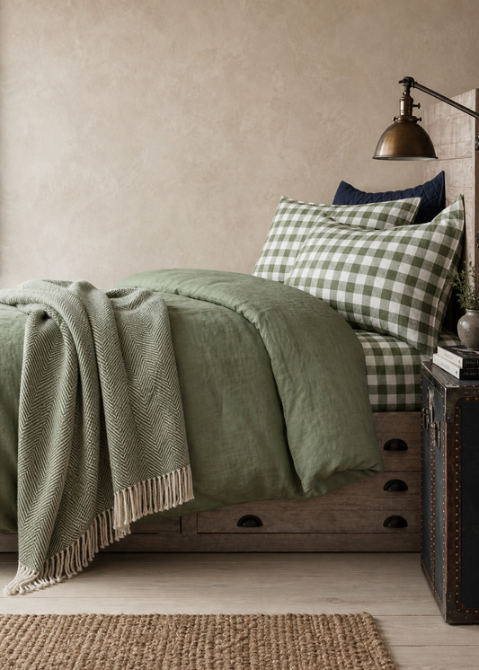 Bedroom with green bedding and plaid pillows against a beige wall.