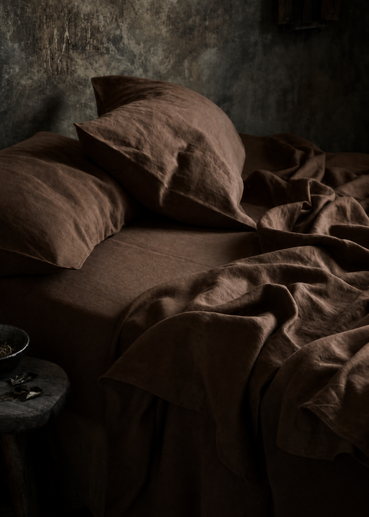 Dark bedroom with a bed covered in brown sheets and pillows.