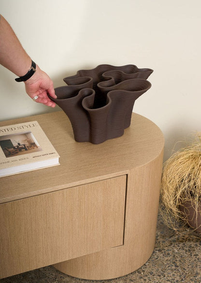 Ceramic vase being placed on a wooden side table with a neutral background