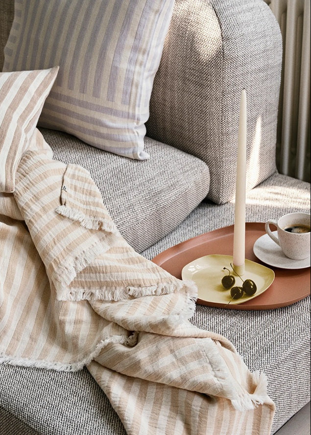 Cozy living room scene with a gray sofa, striped cushions, and a candle on a side table.