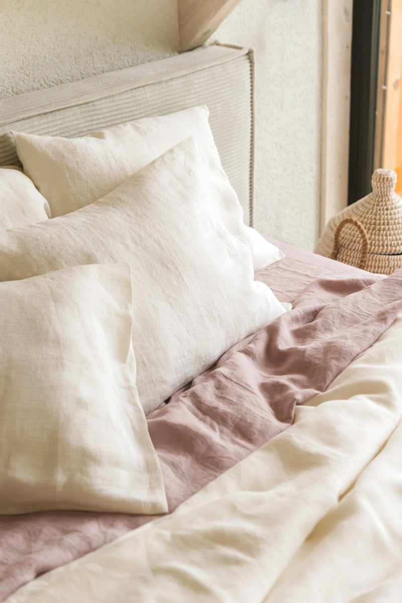 Neatly made bed with white pillows and pink blanket in a softly lit room.