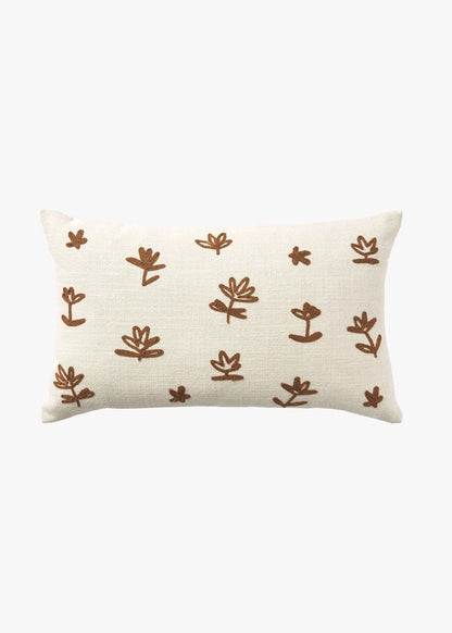 A rectangular cream-colored throw pillow with a textured linen-like fabric, decorated with a repeating pattern of hand-drawn brown botanical motifs, shown against a plain white background.