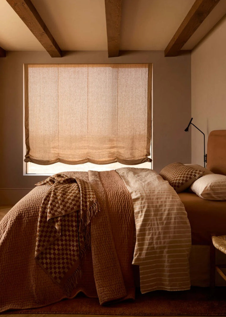 Cozy bedroom with a bed covered in blankets, a lamp, and a window with a curtain.
