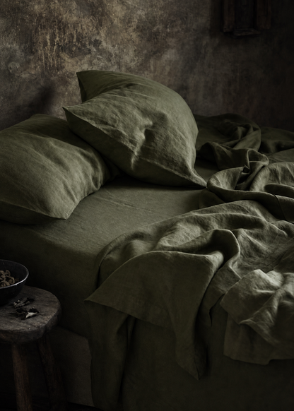 Dark room with a bed covered in green bedding and pillows.
