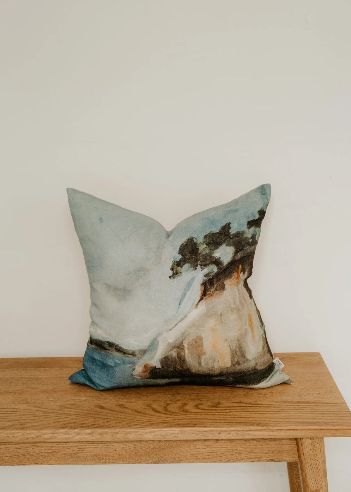 Decorative pillow with a nature design on a wooden bench against a white wall