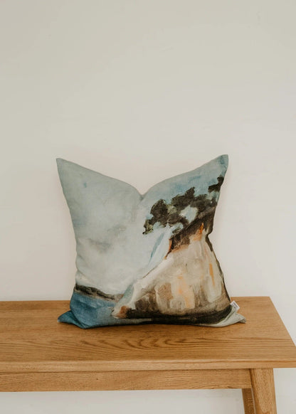 Decorative pillow with a nature design on a wooden bench against a white wall