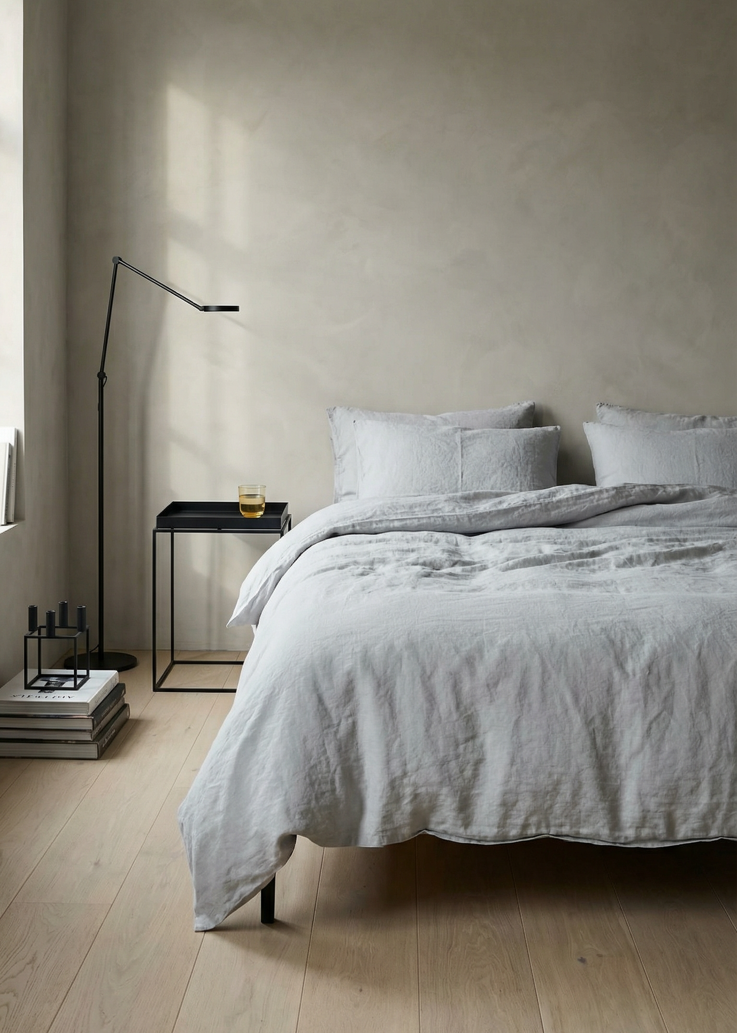 Neatly made bed with light gray bedding in a minimalistic bedroom.