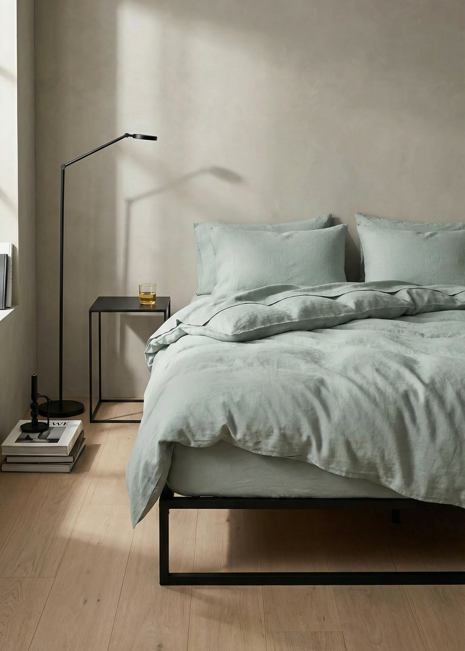 Neatly made bed with light green bedding in a minimalistic bedroom.