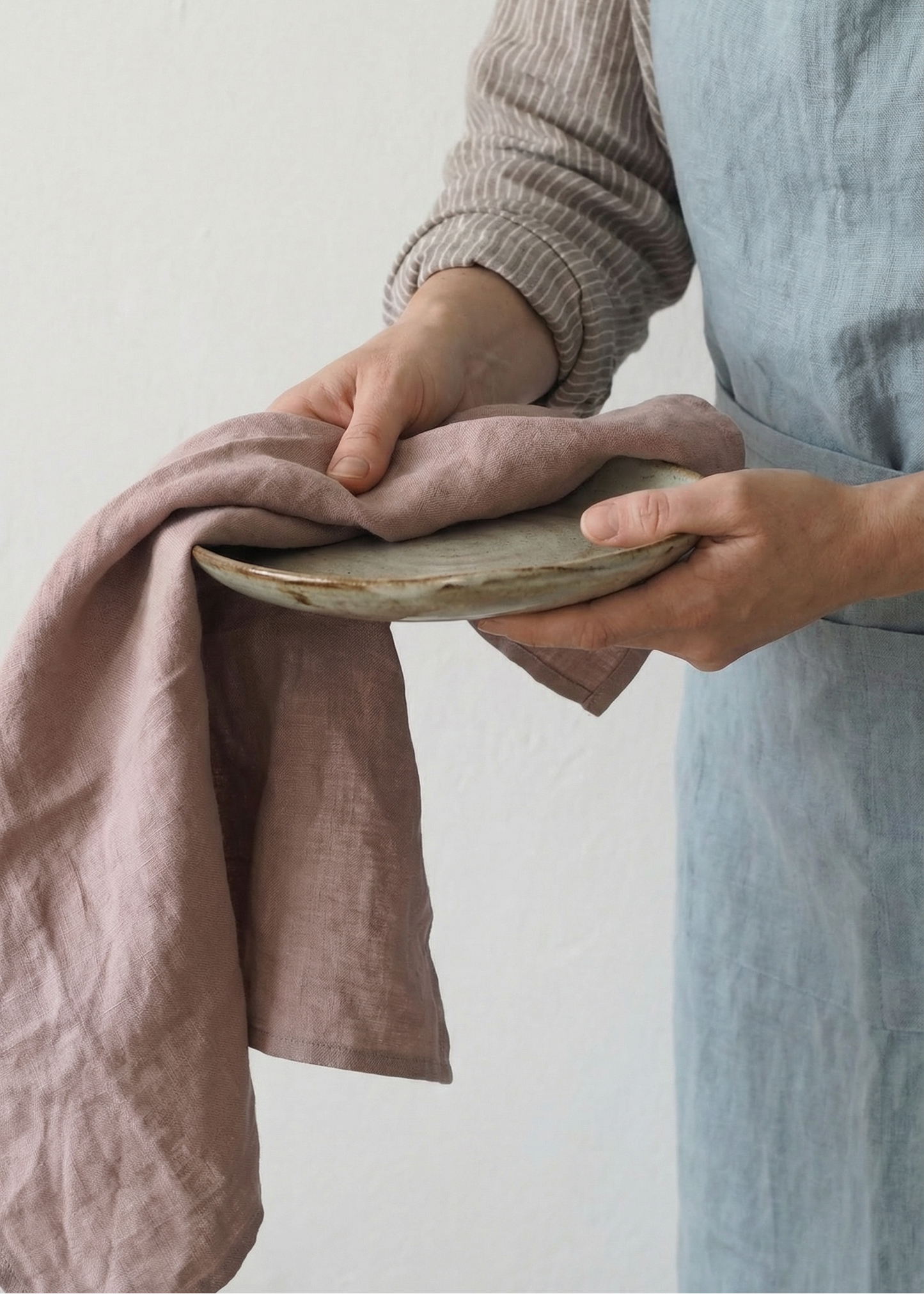 Person holding a ceramic plate with a pink cloth against a plain background