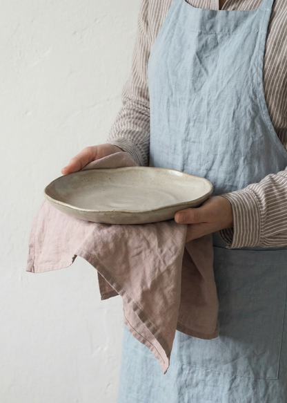 Person holding a ceramic plate with a light blue apron and pink towel.