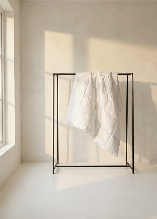 Black metal clothing rack with white garment against a neutral wall.