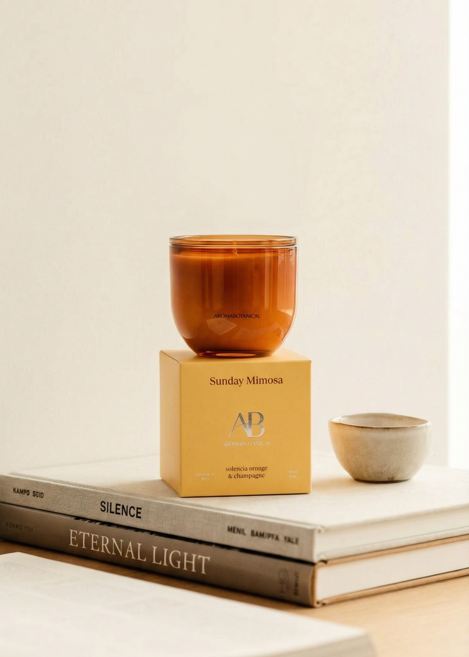 Candle in a amber glass on top of books with a light background