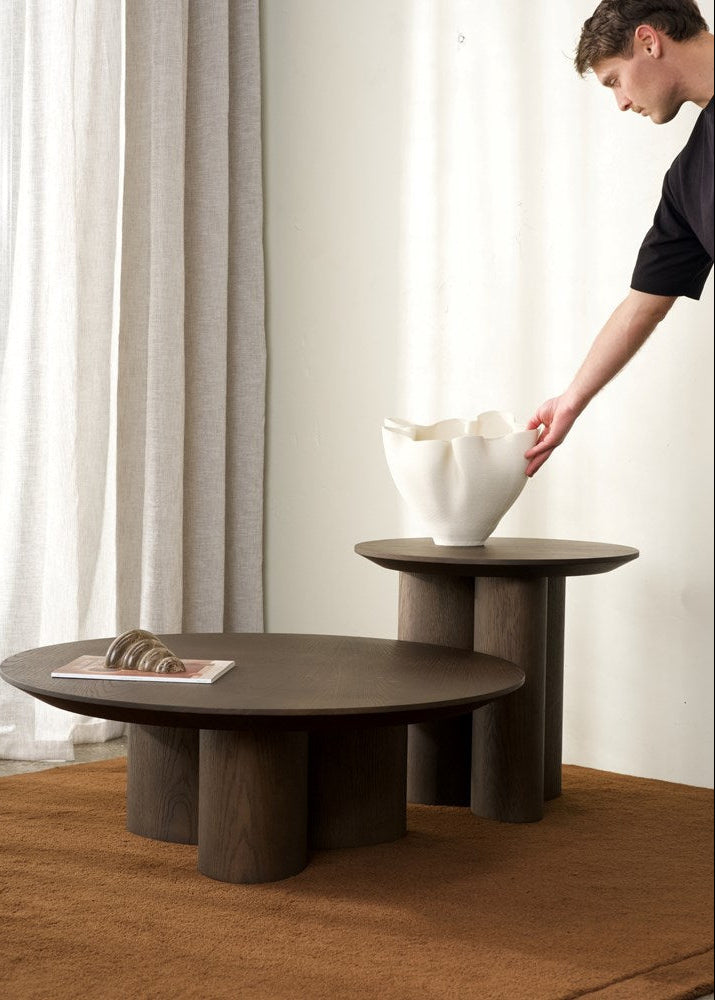 Person placing a white vase on a wooden table with a minimalistic background