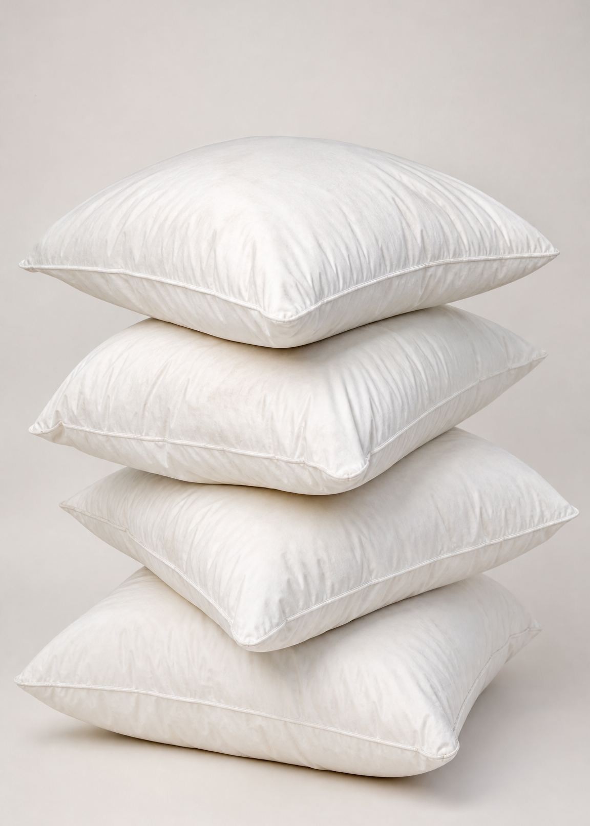 Four white square pillows stacked vertically on a light beige studio background.