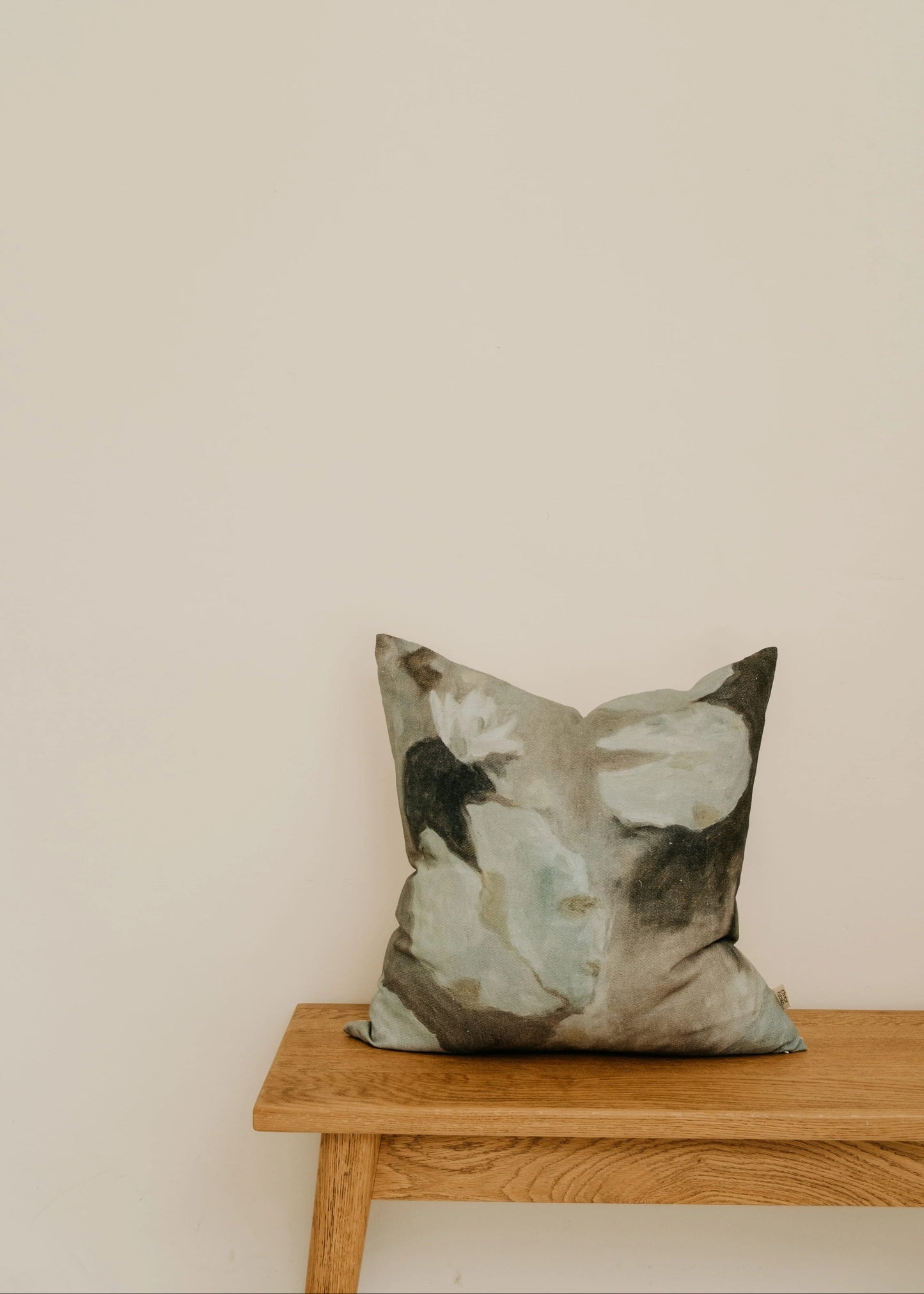 Decorative pillow with abstract design on a wooden bench against a beige wall