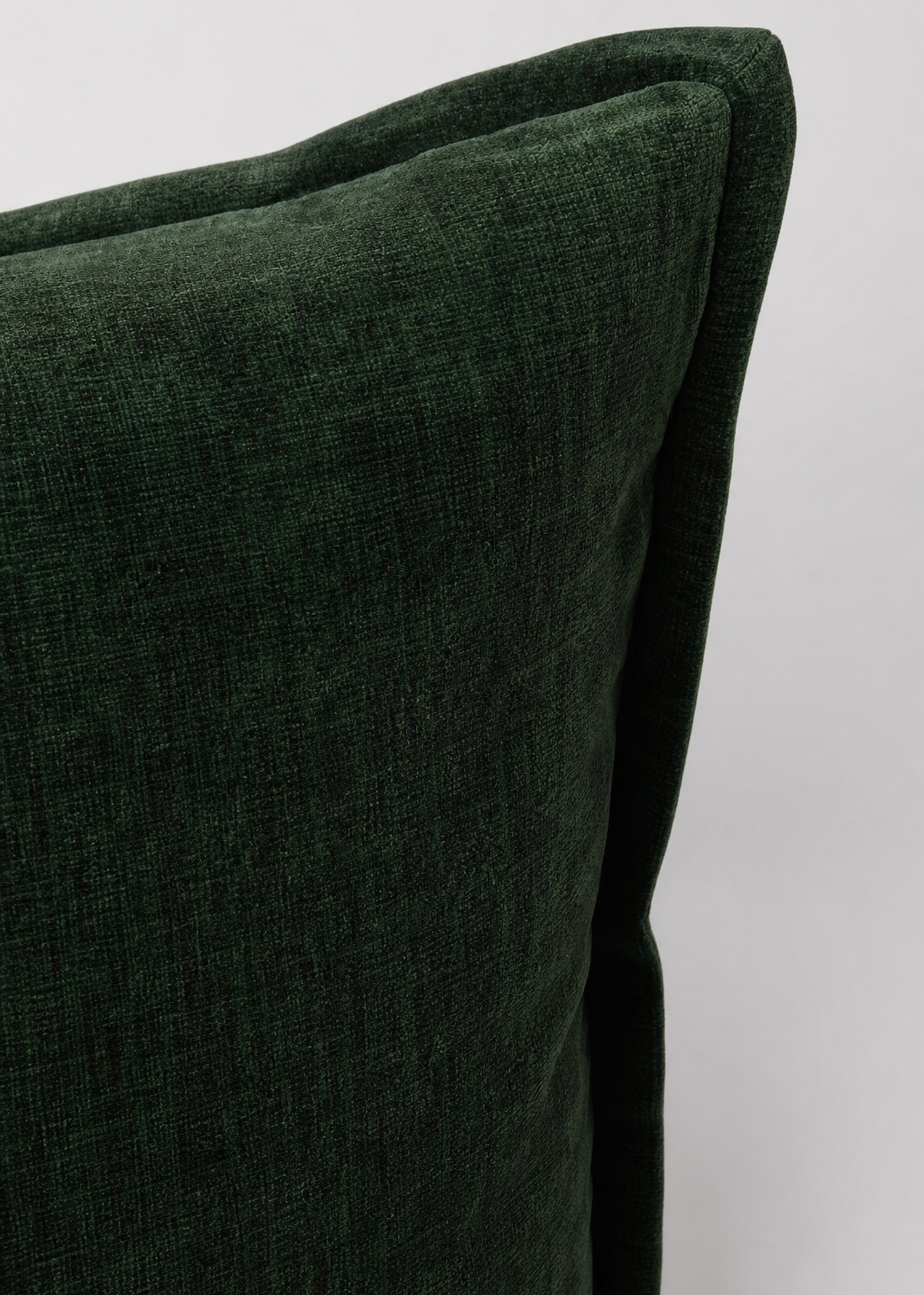 Close-up of a dark forest green textured fabric cushion corner on a light gray background.