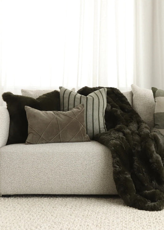 Gray sofa with decorative pillows and a dark fur throw in a neutral setting