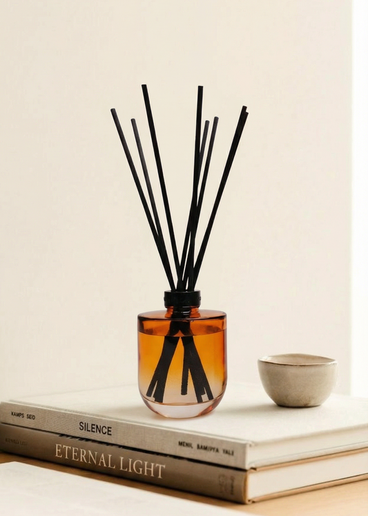 Reed diffuser with black sticks in an amber glass container on a stack of books.