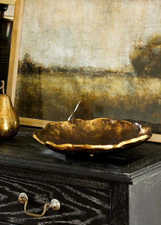 Decorative gold bowl on a dark wooden surface with a textured wall in the background
