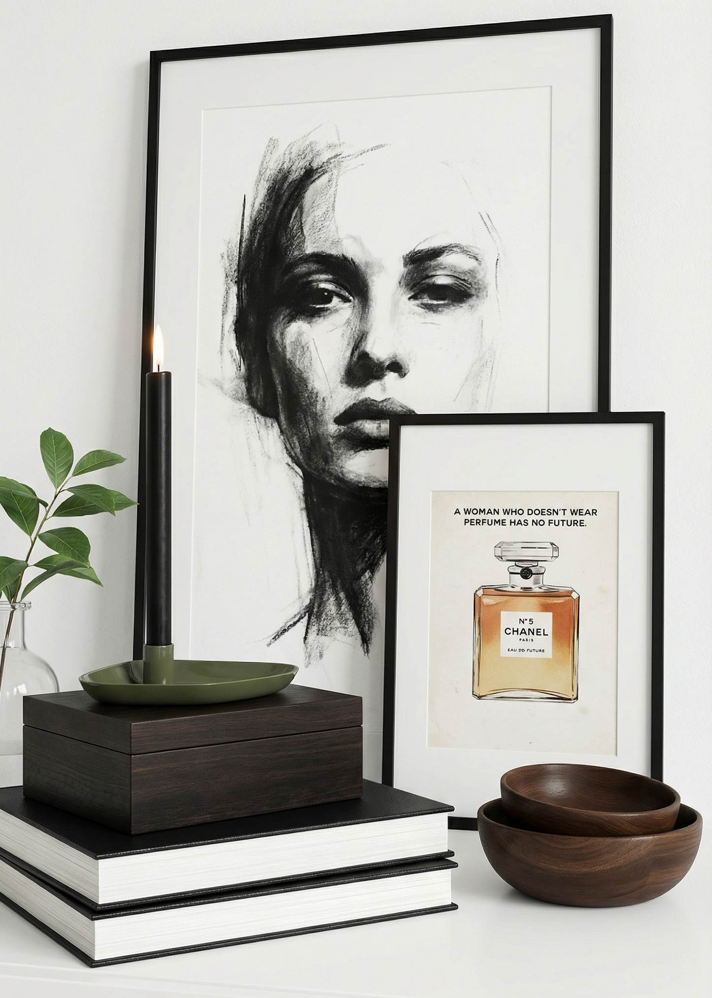 Framed artwork of a woman's face and a Chanel perfume bottle on a white surface with books and a plant.