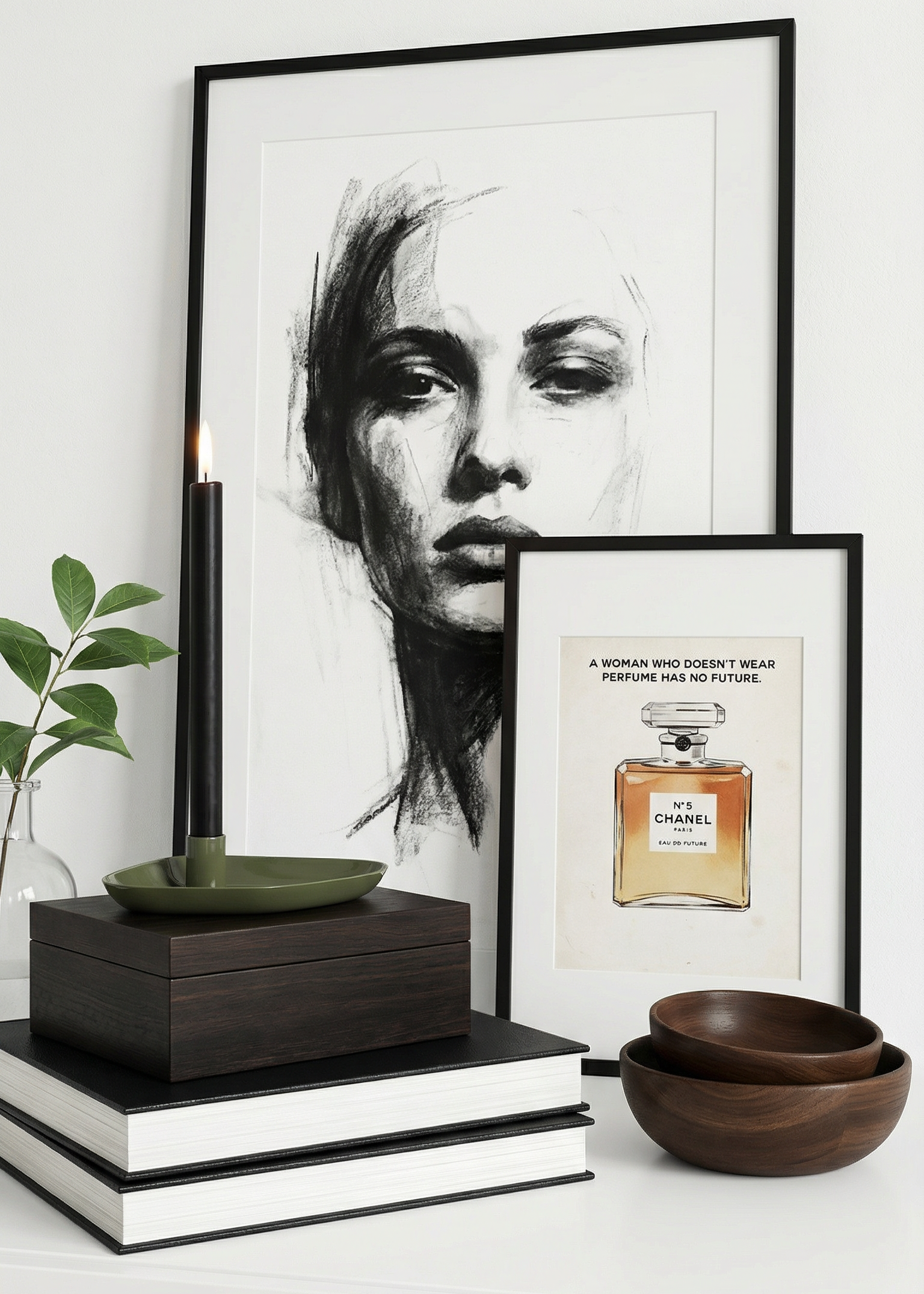 Framed artwork of a woman's face and a Chanel perfume bottle on a white surface with books and a plant.
