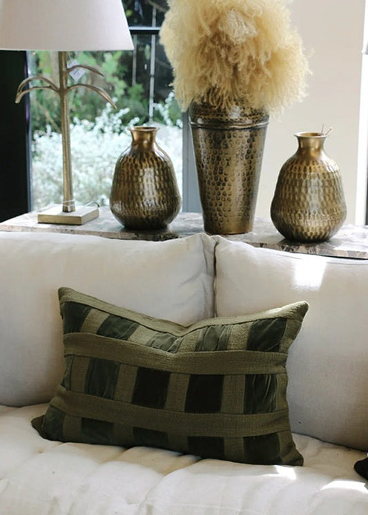 Decorative pillow on a white sofa with decorative vases and lamp in the background.
