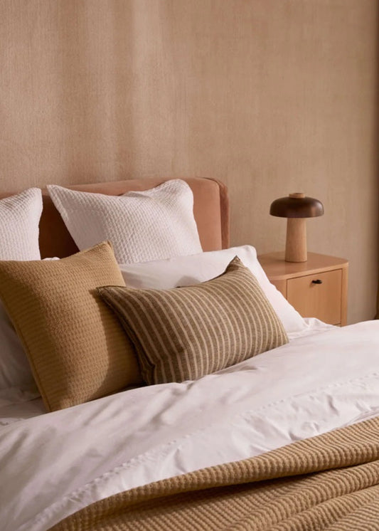 Bed with white bedding and brown and beige pillows against a beige wall.