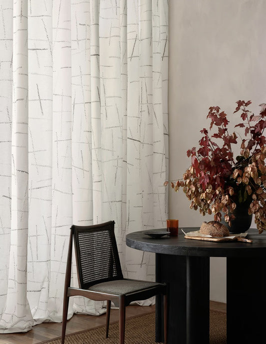 Dining room with a table, chair, and decorative plant against a curtain.