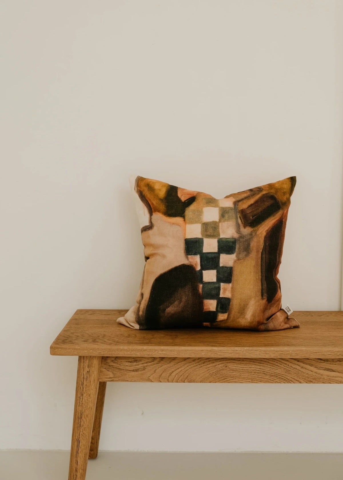 Decorative pillow with a checkered pattern on a wooden bench against a plain wall.