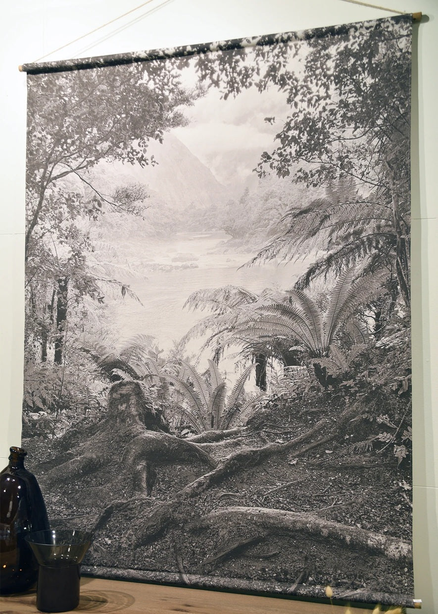 Tapestry of a forest scene hanging on a wall with a wooden shelf below.