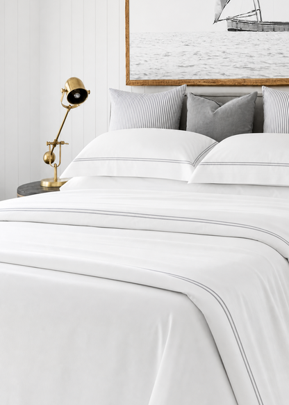 Neatly made bed with white bedding and gray pillows, side table with lamp, and framed artwork on the wall.