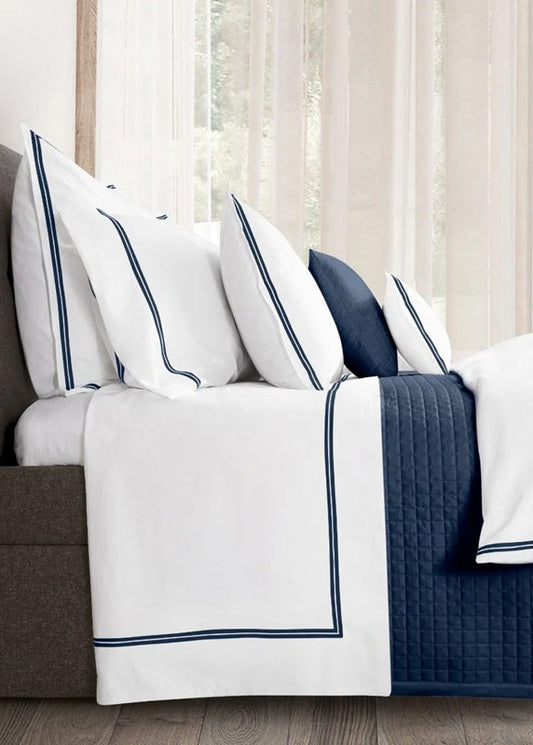 Bed with white and blue bedding in a room with large windows.