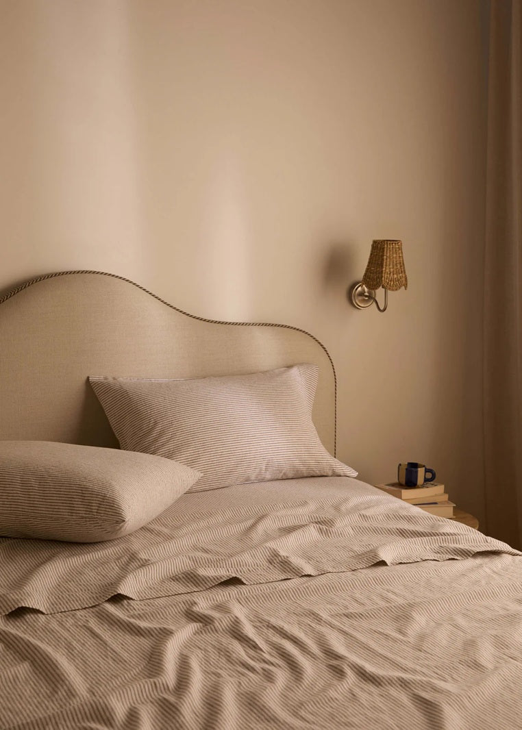 Neatly made bed with beige bedding and pillows in a softly lit bedroom.