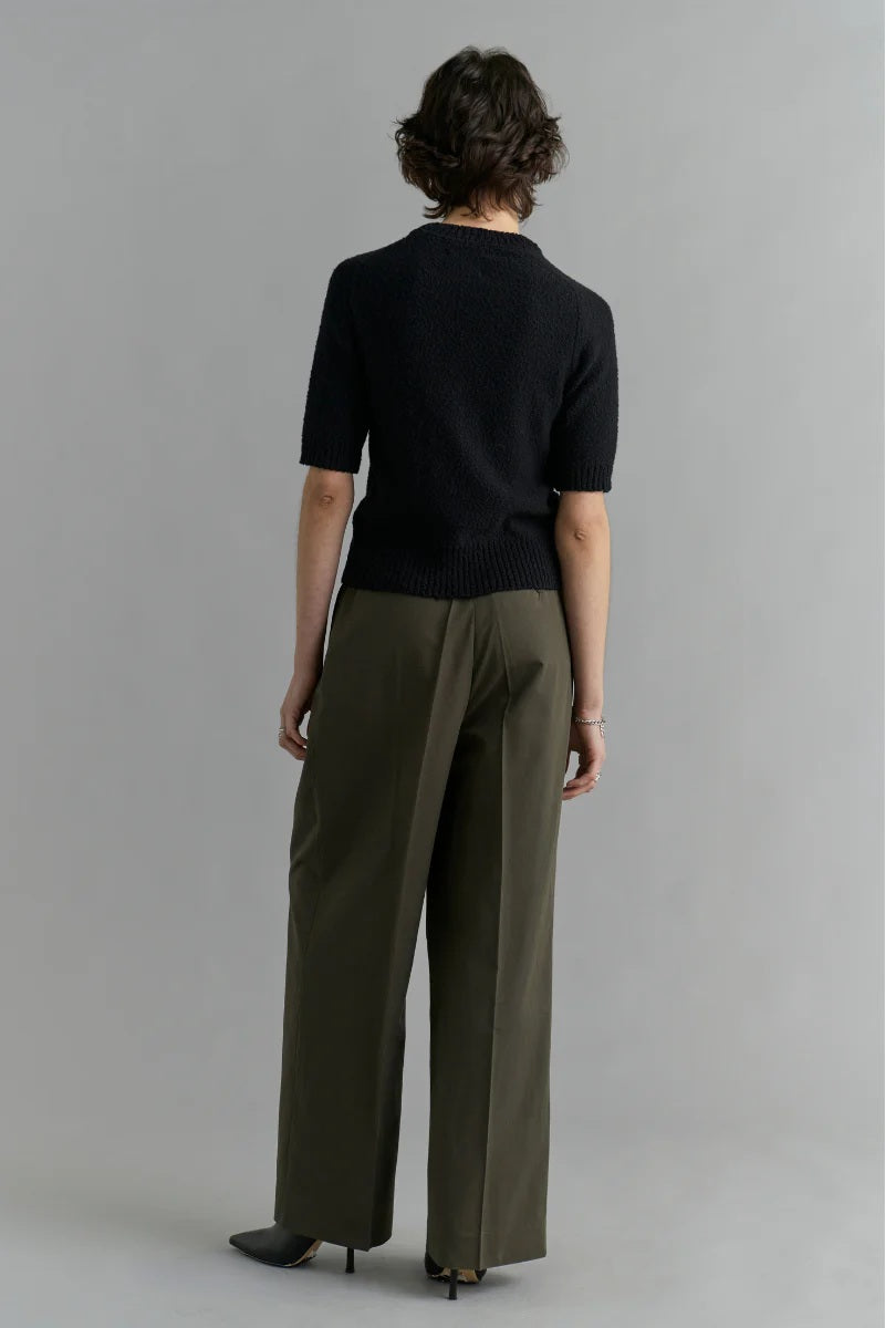 Person wearing a black top and green pants against a gray background