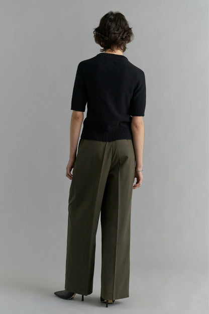 Person wearing a black top and green pants against a gray background