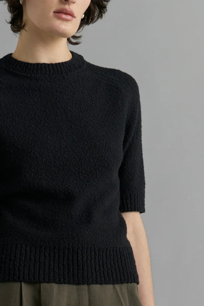 Person wearing a black knit sweater against a gray background