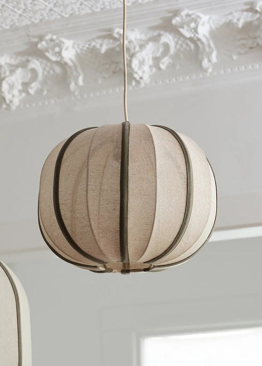 Round beige pendant light hanging against a decorative white wall.