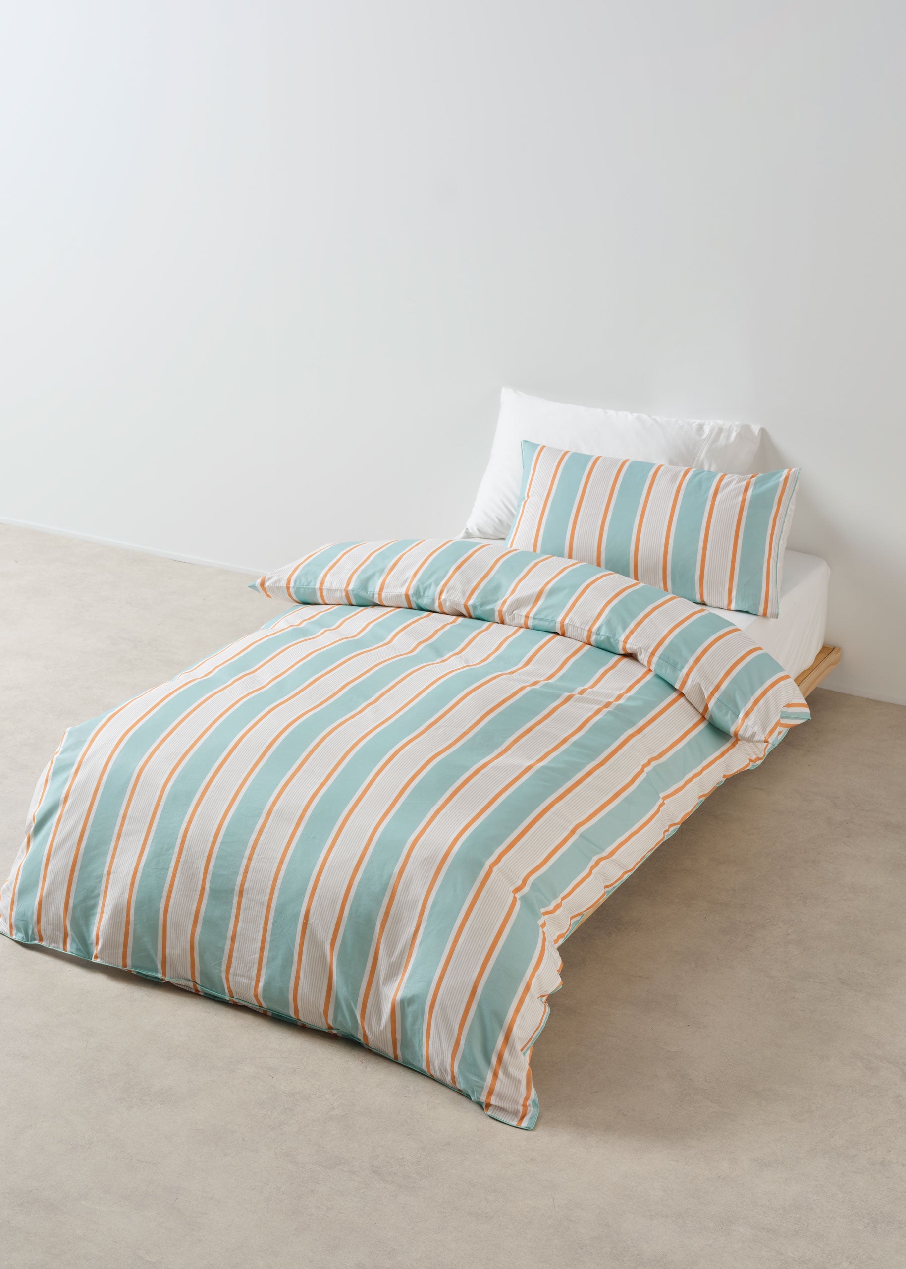 Striped bedspread with matching pillow on a bed against a white wall