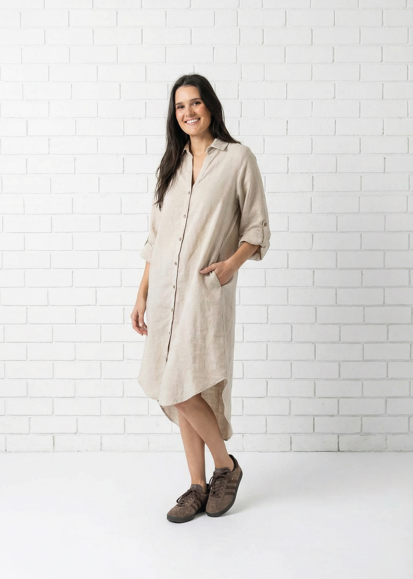 Woman wearing a beige shirt dress against a white tiled wall