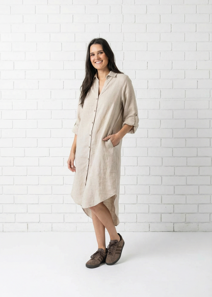 Woman wearing a beige shirt dress against a white tiled wall