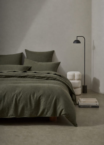 Minimalist bedroom with green bedding and a lamp against a gray wall.