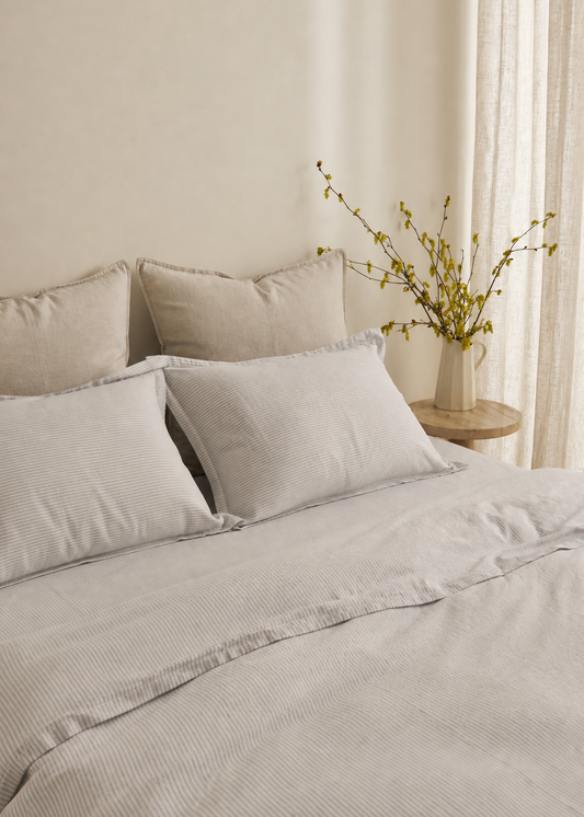 Neatly made bed with light gray bedding in a bedroom setting.